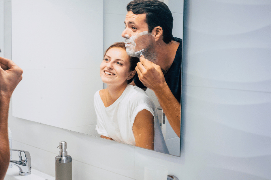 Man and woman in bathroom mirror. Man Shaving.